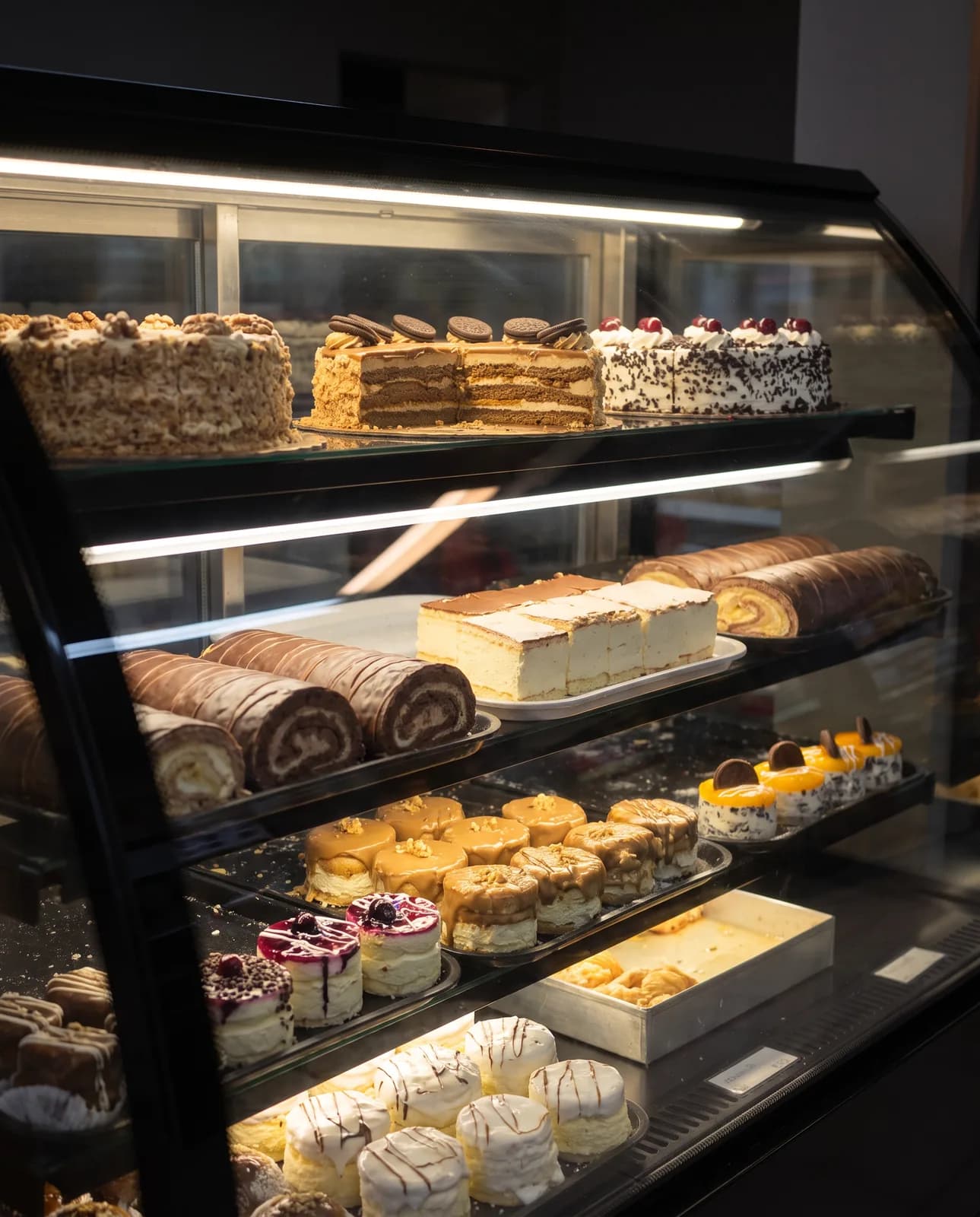 Tortenvitrine mit Schnitten, Rouladen und kleinen Törtchen