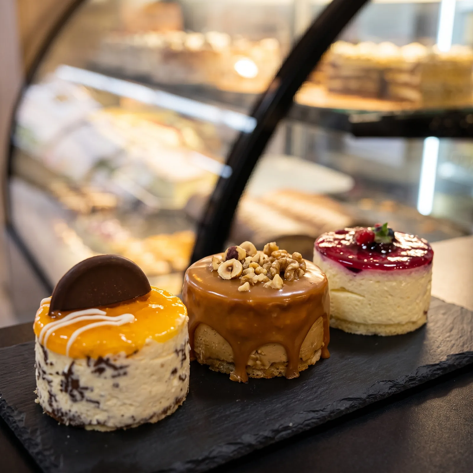 Drei Mini-Torten mit Karamell, Beeren und Orange auf einer Schieferplatte