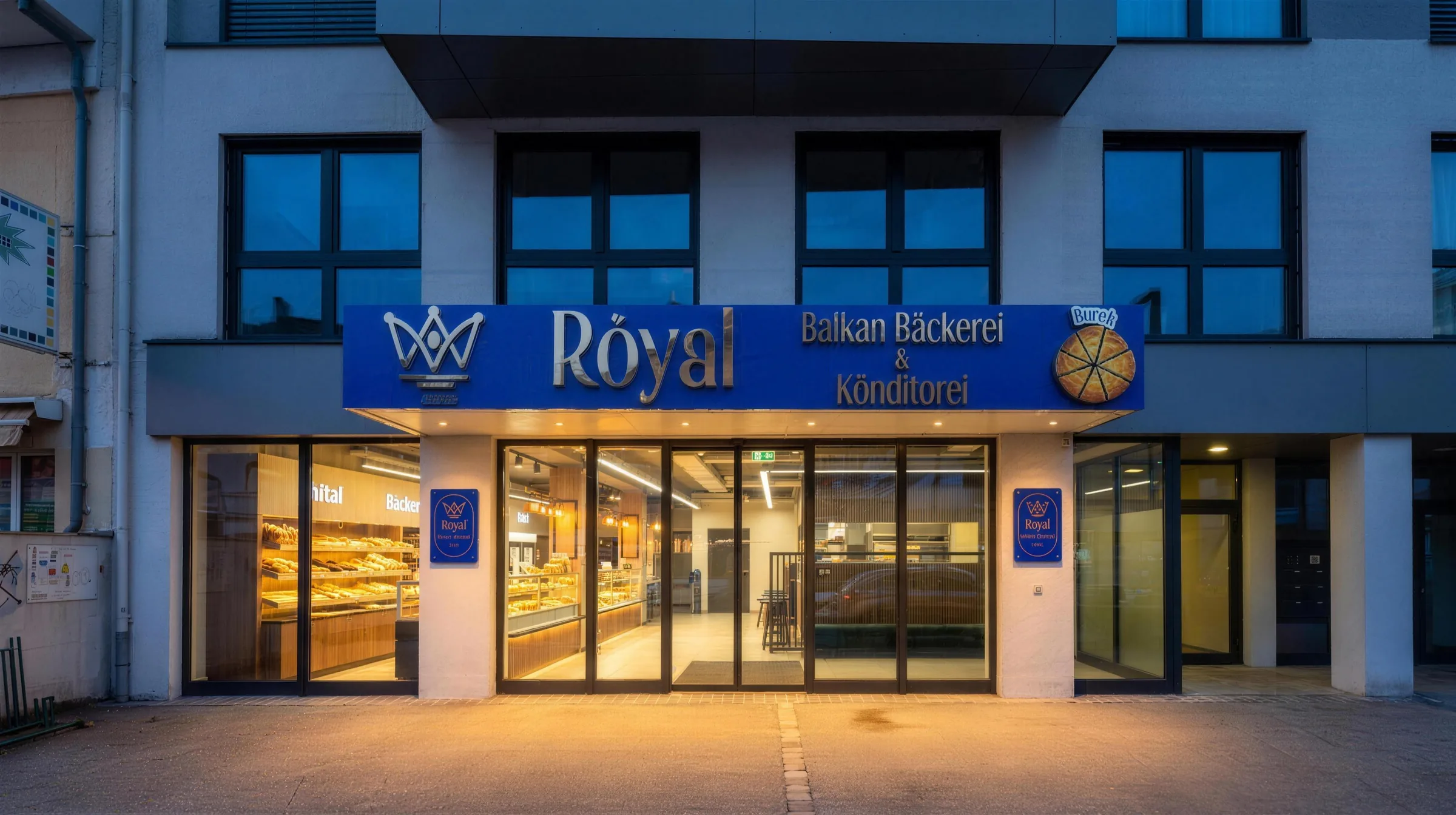 Die beleuchtete Fassade der Royal Balkan Bäckerei an der Hauptstraße in Mödling am Abend